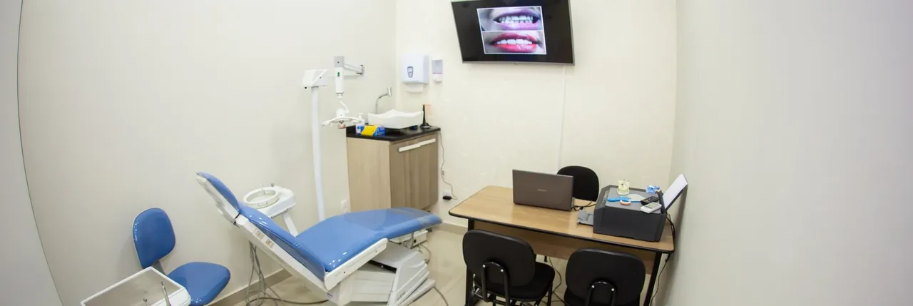 Consultório com cadeira odontológica, equipo, refletor e bancada de trabalho ao lado