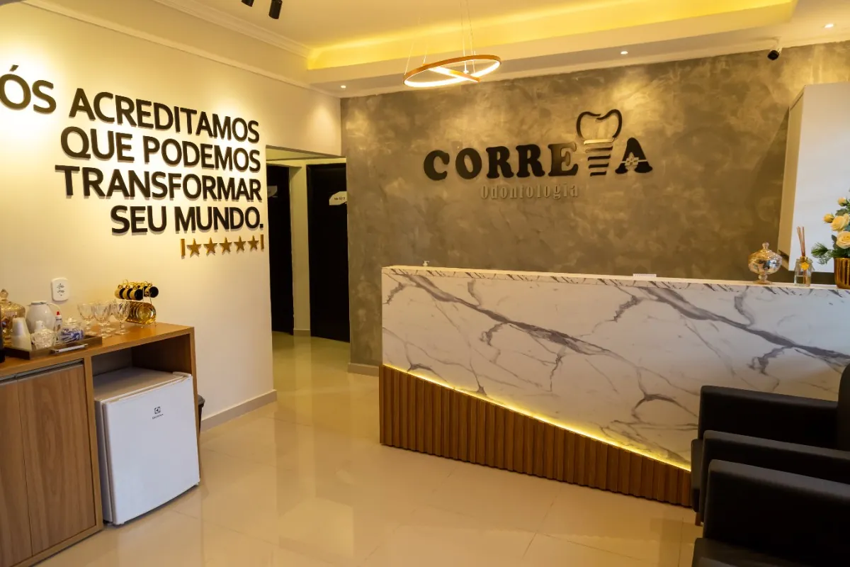 Recepção da clínica: balcão de mármore claro com o logotipo da Correia Odontologia na parede de fundo e luminária circular no teto