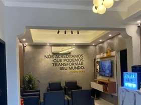 Recepção da unidade de Jales: poltronas escuras, televisão na parede e o logotipo aplicado sobre a frase "Nós acreditamos que podemos transformar seu mundo"